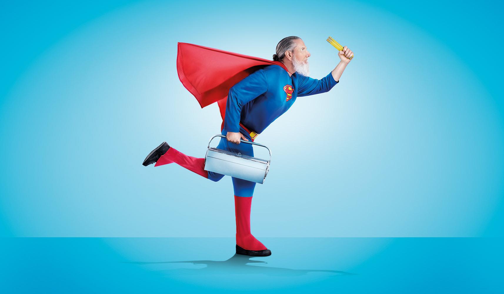 Bärtiger Mann im Superman-Kostüm mit Werkzeugkoffer im Laufschritt