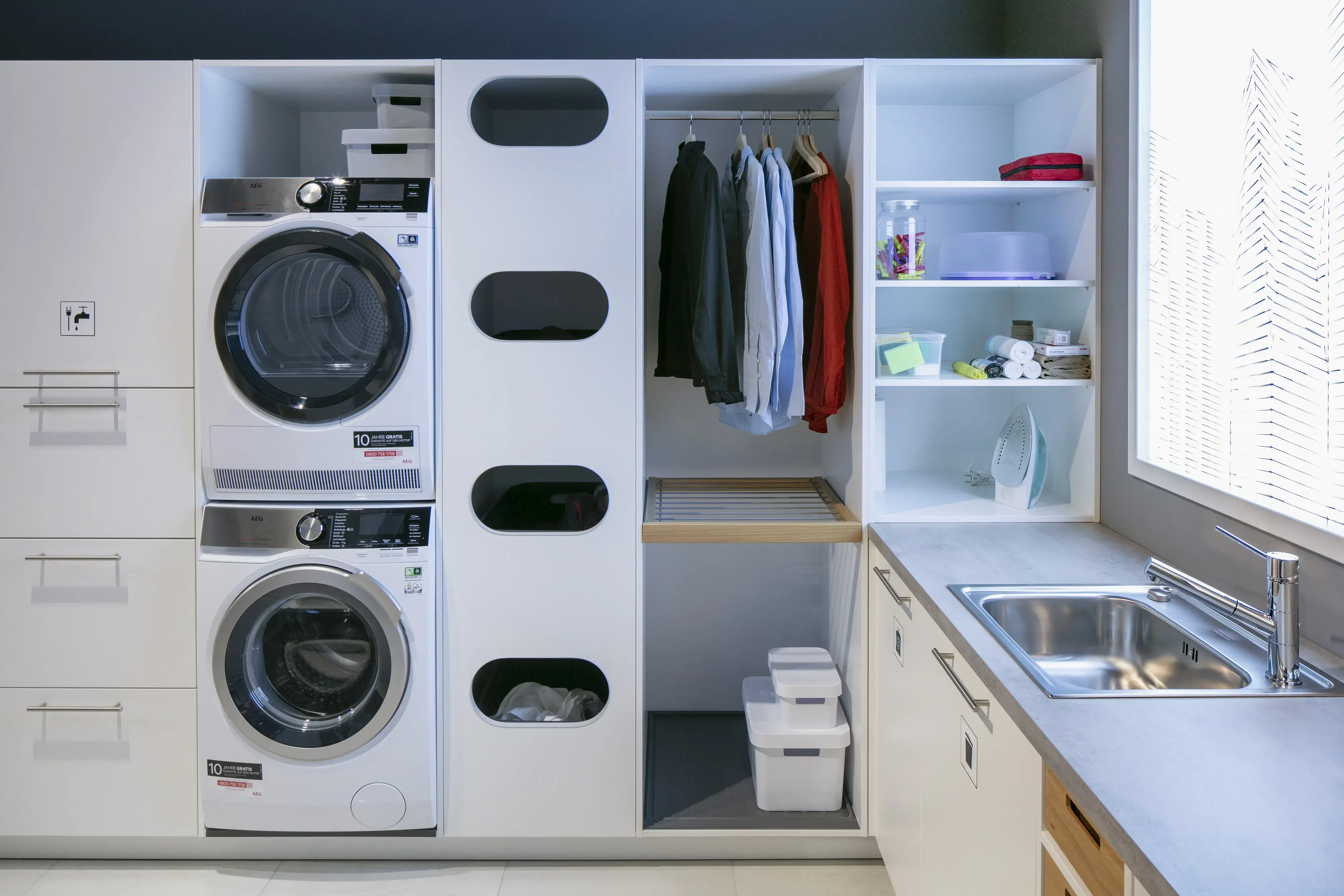 Hauswirtschaftsraum mit Waschmaschine und Trockner übereinander und Spülbecken Möbel von Schüller Küchen